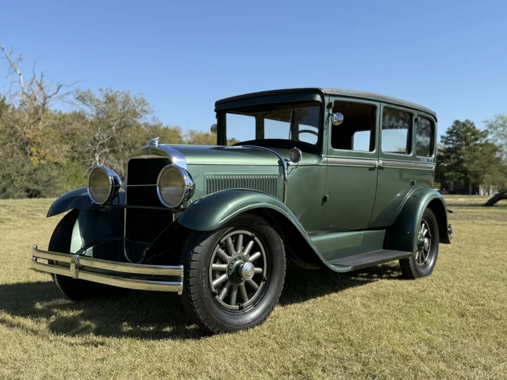 1928 Studebaker Dictator Sedan Lady Gatsby – front passenger-side angle showing chrome headlights, classic fenders, and forest green body, SpeedNut Classic Car Rentals.