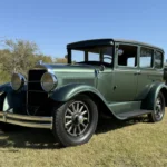 1928 Studebaker Dictator Sedan Lady Gatsby – front passenger-side angle showing chrome headlights, classic fenders, and forest green body, SpeedNut Classic Car Rentals.