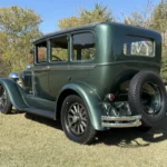 1928 Studebaker Dictator Sedan Lady Gatsby – rear driver-side view with spare tire mounted on the back, forest green exterior, SpeedNut Classic Car Rentals.
